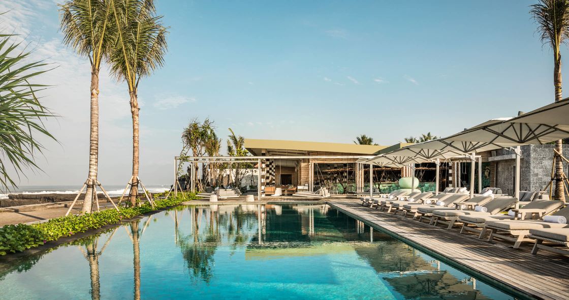 A Swimming Pool With Lounge Chairs And A Building With Trees In The Background