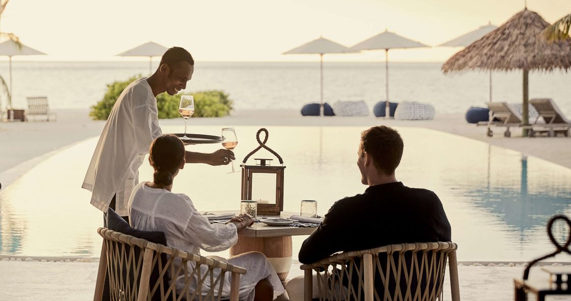 A Group Of People Sitting On A Bench Next To A Body Of Water