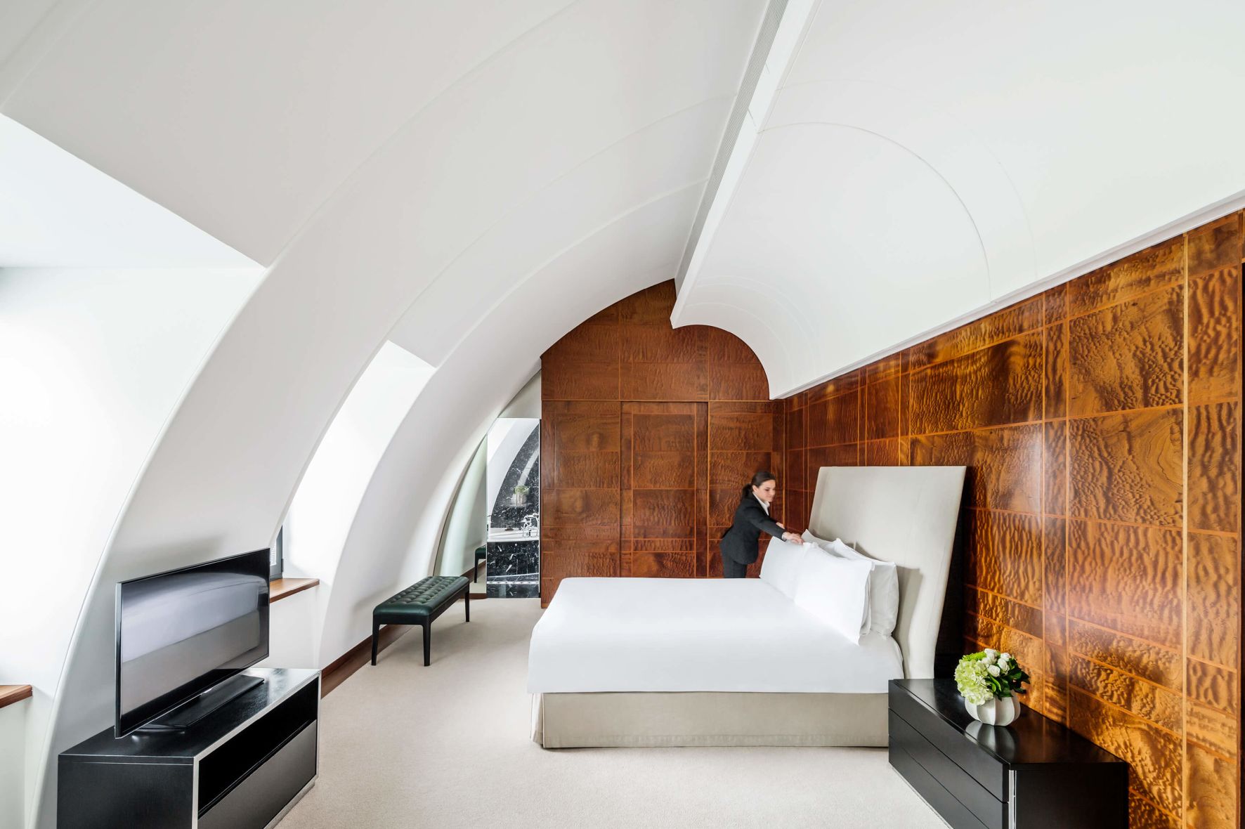 A Person Sitting On A Bed In A Room With A Wood Wall