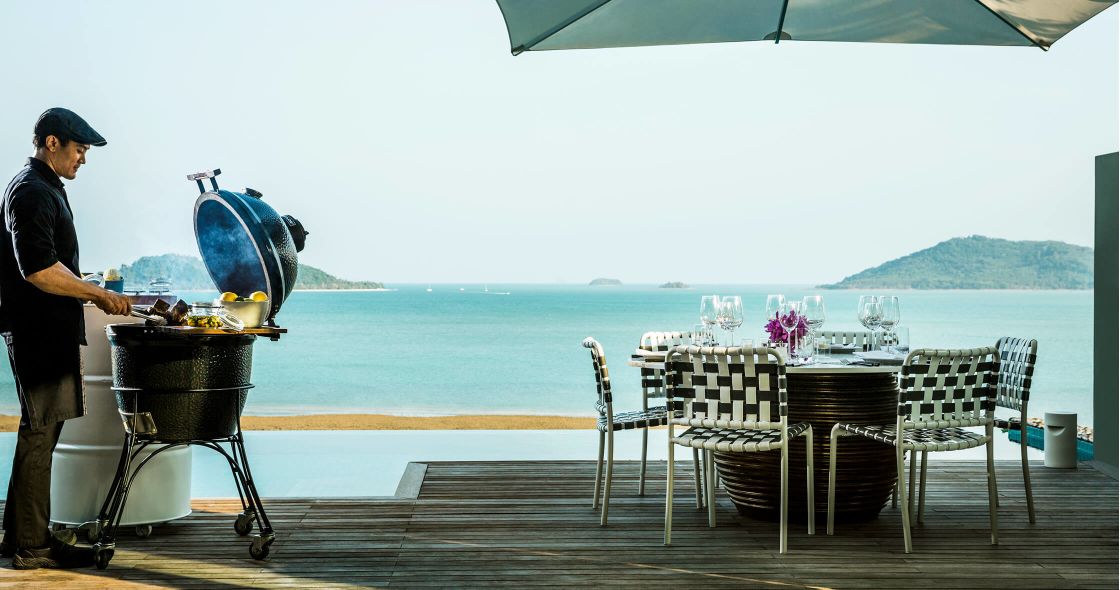 A Person Standing Next To A Table With Chairs And A Grill On A Dock By The Water