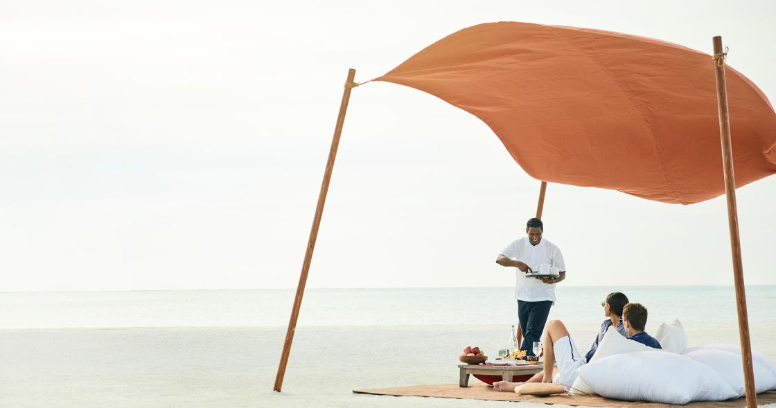 A Man Standing Next To A Couple Of Women Sitting On A Beach