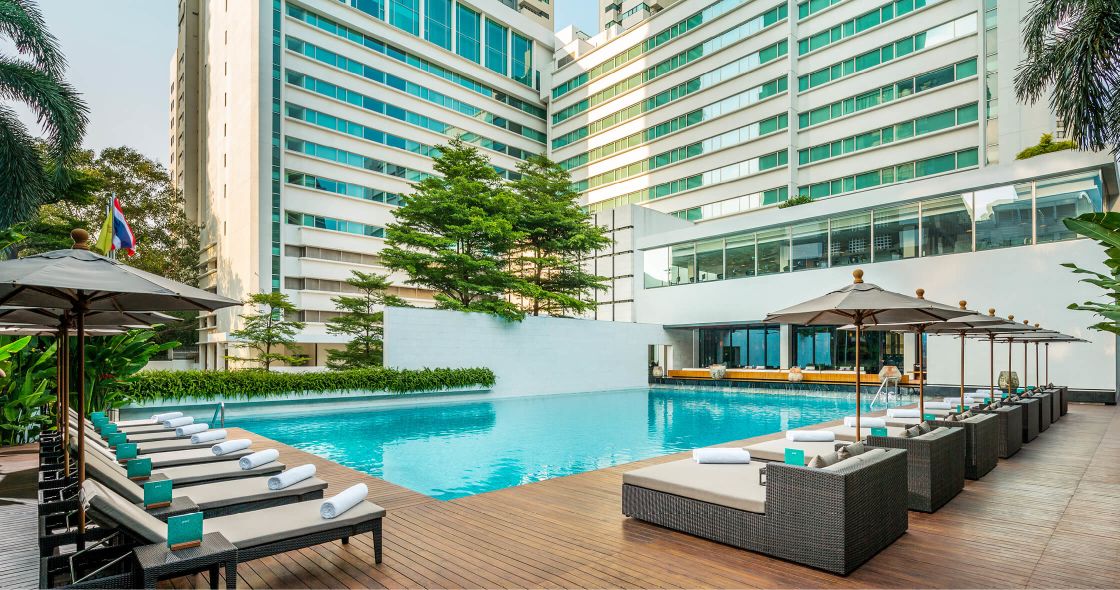 A Pool With Lounge Chairs And Umbrellas Next To A Building