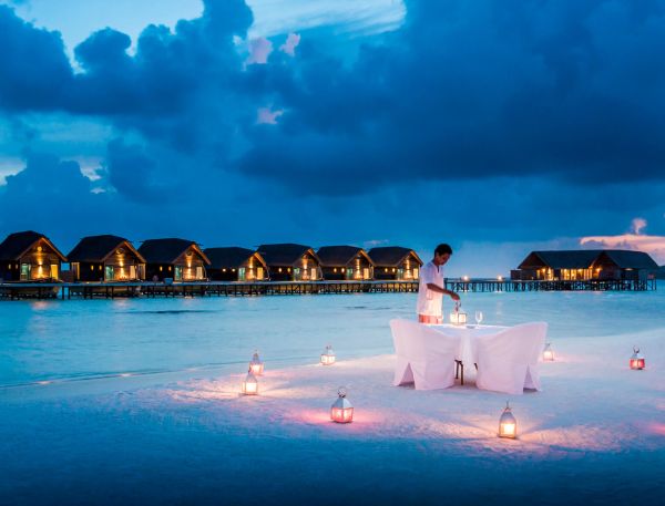 A Person Standing On A White Platform Surrounded By Water With A Row Of Lit Up Buildings In The