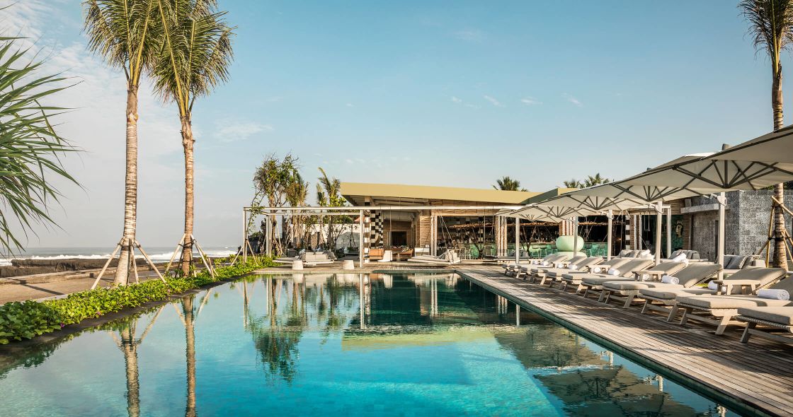 A Swimming Pool With Lounge Chairs And A Building With Trees In The Background