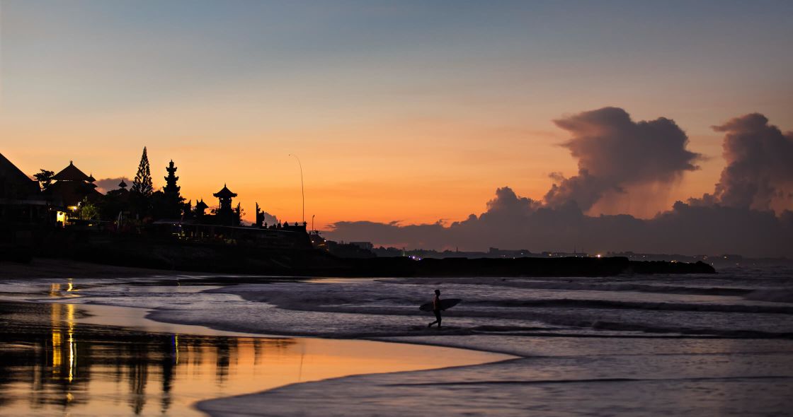 A Person Carrying A Surfboard On A Beach