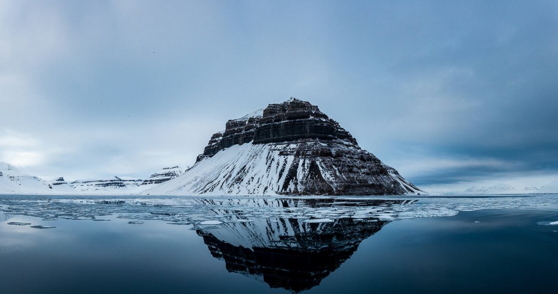 A Snowy Mountain With A Body Of Water Below