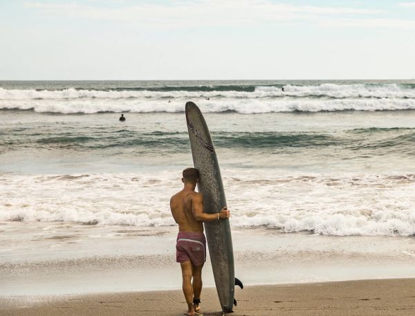 A Man Holding A Surfboard On A Beach