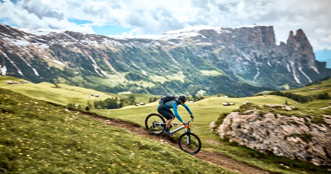 A Person Riding A Bike On A Trail In A Valley With Mountains In The Background