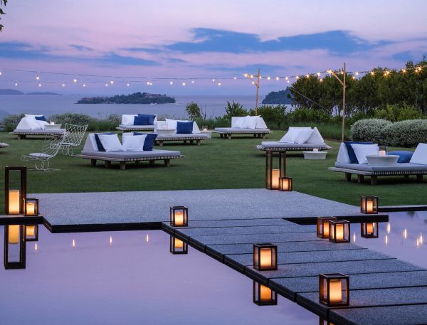 A Pool With Lounge Chairs And Umbrellas By A Body Of Water