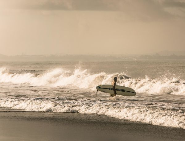 A Man Carrying A Surfboard On A Beach