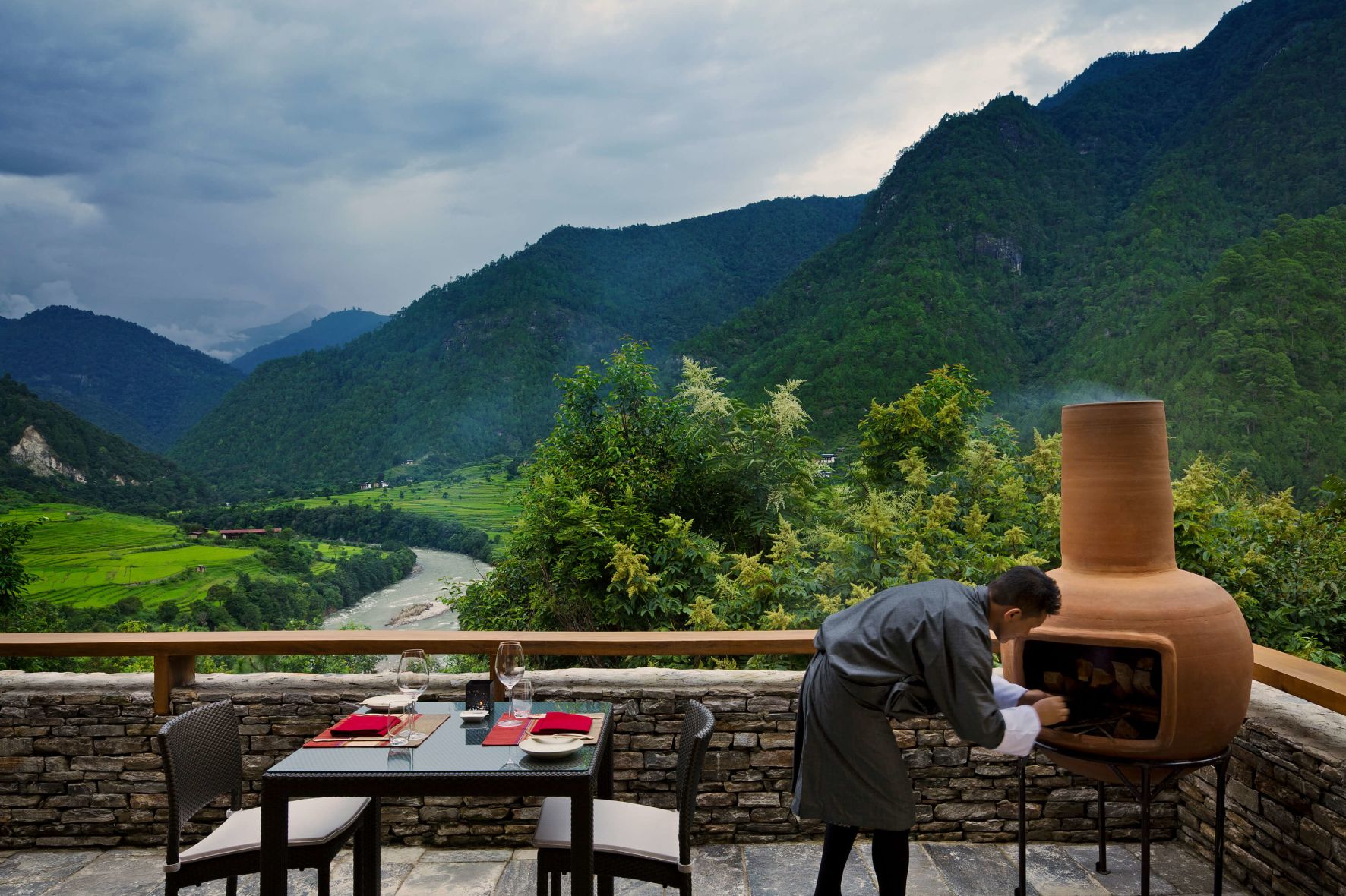 A Person Standing On A Balcony Overlooking A Valley With Mountains In The Background